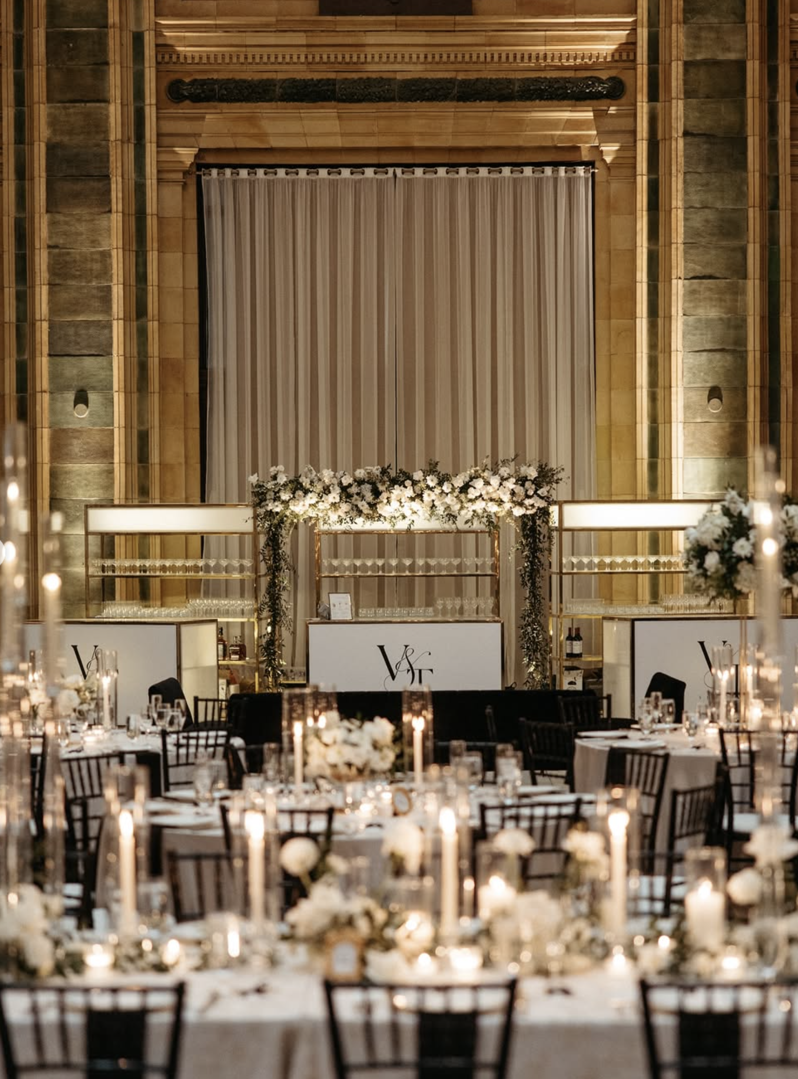 A pittsburgh wedding venue lit by candles, at the end of the tables theres a bar with white florals